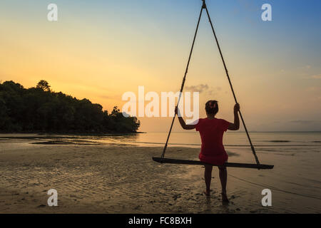 Frau sitzen auf Swing Bar Blick bei Sonnenuntergang am Strand Stockfoto