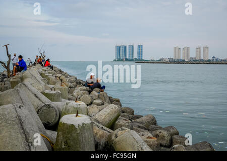 Menschen, die von Tetrapoden-Strukturen fischen, die den Fischereihafen Muara Angke als Wellenbrecher in Penjaringan, Jakarta, Indonesien, schützen. Stockfoto