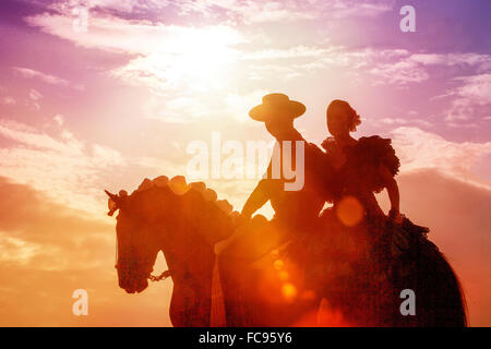 Lusitano. Paar im spanischen Kostüm, Reiten auf einem Feria, Silhouette gegen einen dramatischen Himmel. Deutschland Stockfoto