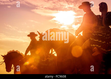 Lusitano. Paare in spanischer Tracht Reiten auf eine Feria, Silhouette gegen einen dramatischen Himmel. Deutschland Stockfoto