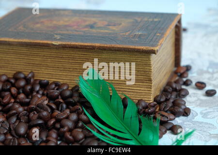 Geröstete Kaffeebohnen, altes Buch und eine grüne Feder Stockfoto