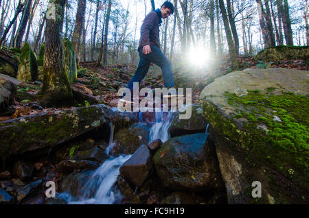 Ein Wanderer Hopfen über plätschernden Kaskaden und tritt über Bergpässe Vegetation erstickt. Stockfoto