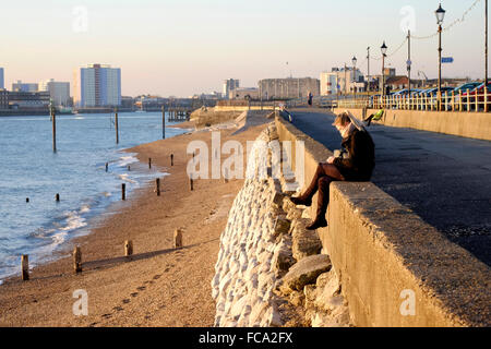 junge Frau saß im goldenen Licht des Sonnenuntergangs auf Southsea Seafront England uk Stockfoto