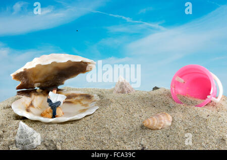 Miniatur Puppe Mann liest Zeitung am Strand beklebt für die Sonne von Sonnenschirm aus Fisch Muschel gefertigt Stockfoto