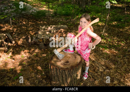 Junges Mädchen halten eine Axt und neben einem Baumstumpf oder Hackstock im Wald stehen, selbstbewusst in die Kamera schaut. Stockfoto