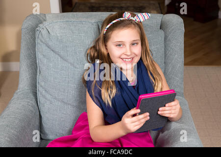 Junges Mädchen im rosa Kleid mit einem e-Book-Reader oder Tablet.  Sie lächelt und das Tablet ist farblich mit ihrem Outfit. Stockfoto