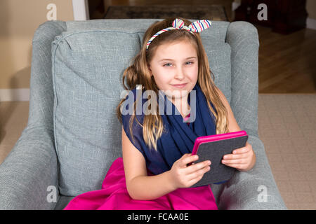 Junges Mädchen im rosa Kleid mit einem e-Book-Reader oder Tablet.  Das Mädchen sucht aus dem Gerät mit einem ernsten Ausdruck. Stockfoto