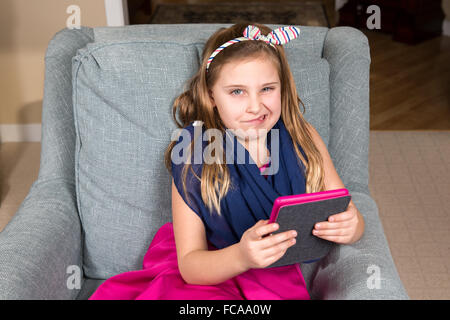 Junges Mädchen im rosa Kleid mit einem e-Book-Reader oder Tablet.  Das Mädchen ist verzog das Gesicht, als sie oben aus dem Gerät schaut. Stockfoto