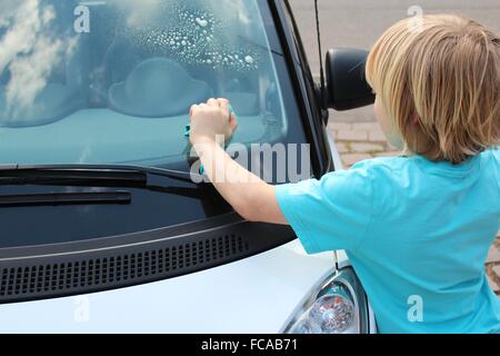 Kind reinigt die Frontscheibe eines Autos Stockfoto