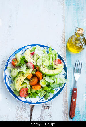 Gesunden Avocado und Gemüse Salat mit Radieschen, Tomaten, Salat, Zwiebeln, Gurken und Karotten auf Holztisch Stockfoto