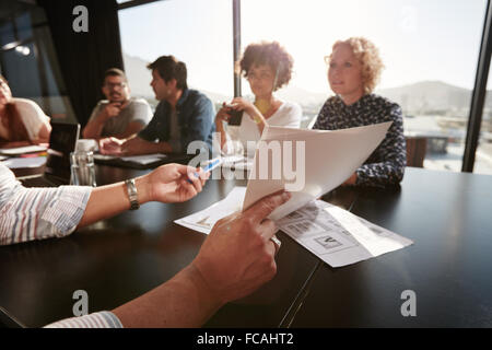 Papiere in Händen des jungen Mannes, Businessplan, seinem Kreativteam zu erklären. Kreativ-Profis treffen im Büro. Stockfoto