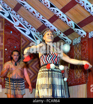 Maori-Frau und Maori-Mann in Te Puia, Rotorua. Frau tanzt mit POI(s), während der Mann im Versammlungshaus, Nordinsel, Neuseeland, singt Stockfoto