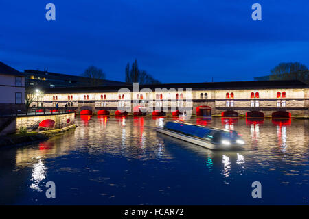 Ausflugsschiff mit Touristen vor der Barrage Vauban (Vauban-Wehr) nachts entlang dem Fluss Ill, Straßburg, Frankreich Stockfoto