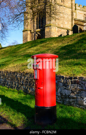 Eine ländliche britische Rote traditionelle Royal Mail Säule Box. Mit St ist Mary Kirche - hinten. In Wymeswold, am 15. Januar 2016. Stockfoto