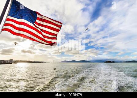 Blick auf die Bucht von San Francisco, Golden Gate Bridge, Möwen, die amerikanische Flagge winken und Alcatraz Island bei Sonnenuntergang von Stockfoto