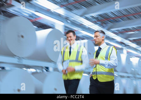 Geschäftsleute in reflektierende Kleidung entlang großer Papier-Spulen in Druckerei Stockfoto