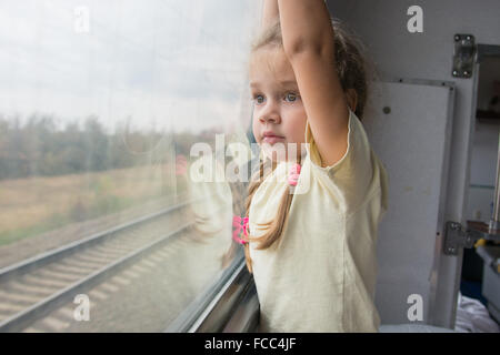 Vierjährige Mädchen schaut aus dem Fenster mit der Unterseite des Regals im Wagen zweiter Klasse Zug Stockfoto