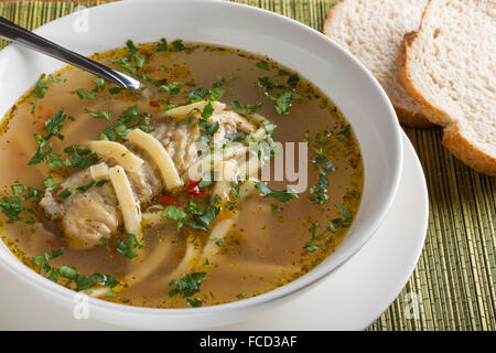 Hausgemachte Hühnersuppe in einer weißen Schüssel mit Löffel und Brot Stockfoto