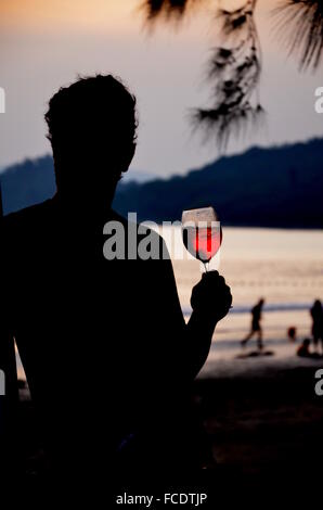 Silhouette der Mann hält Glas Rosé bei Sonnenuntergang am Strand Stockfoto