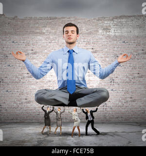 Junger Geschäftsmann in Lotus Pose sitzen und unterstützt durch Kollegen Stockfoto