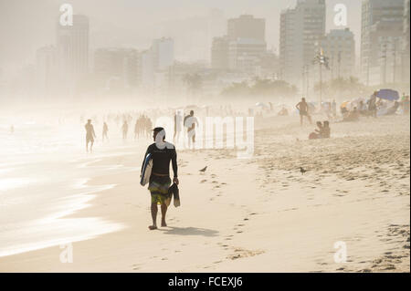 RIO DE JANEIRO - 18. Januar 2014: Surfer Spaziergänge am Strand von Ipanema Strand gegen eine neblige Sicht auf die Skyline der Stadt. Stockfoto