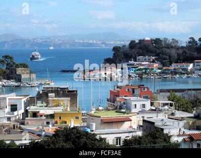 Mit Blick auf den Hafen von Ischia Porto auf tiefstehende Sonne. Die dunkle Farbe des Meeres macht einen schönen Kontrast mit dem helleren Blau des Himmels. Im Hintergrund die Insel Procida Stockfoto