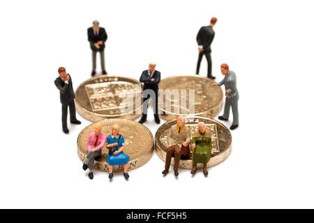 2 Miniatur-Paare sitzen auf britischen Münzen umgeben von Finanzberater in Anzügen Konzept. Stockfoto