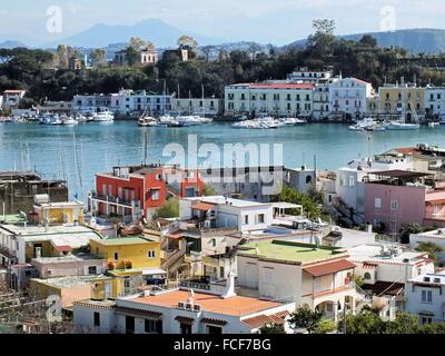 Mit Blick auf den Hafen von Ischia Porto auf tiefstehende Sonne. Die dunkle Farbe des Meeres macht einen schönen Kontrast mit dem helleren Blau des Himmels. Im Hintergrund die Insel Procida und den Vesuv Stockfoto