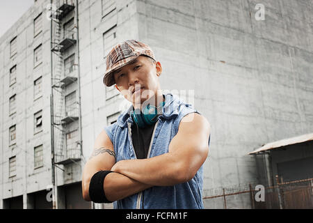 Ein junger Mensch in einem ärmellosen Jeanshemd, verschränkten Armen in die Kamera schaut. Stockfoto