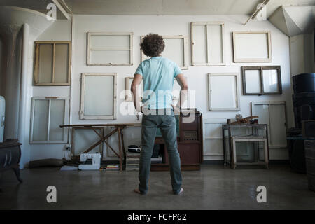 Loft-Dekor. Eine Wand gehangen mit Bilder in Rahmen, umgekehrt, um den Rücken zu zeigen. Ein Mann mit Händen in den Hüften, Blick auf die Wand. Stockfoto