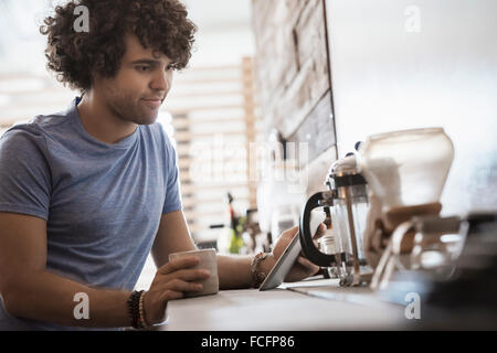 Loft-lebendigen. Ein junger Mann sitzt mit einer Tasse Kaffee, halten eine digitale-Tablette. Stockfoto