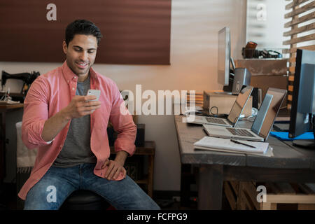 Ein Mann sitzt in einem Büro zu Hause, mit zwei Laptops auf dem Schreibtisch, Überprüfung seiner Smartphone. Stockfoto