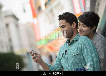 Ein paar, Mann und Frau umarmt auf einer Stadtstraße. Mann hält ein smart Phone. Stockfoto
