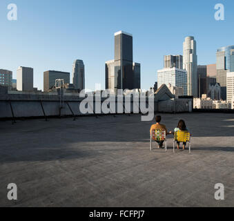 Ein paar, Mann und Frau sitzen in Liegestühlen auf der Dachterrasse mit Blick auf die Wolkenkratzer. Stockfoto