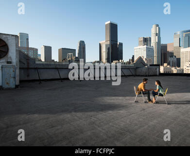 Ein paar, Mann und Frau sitzen in Liegestühlen auf der Dachterrasse mit Blick auf die Wolkenkratzer. Stockfoto