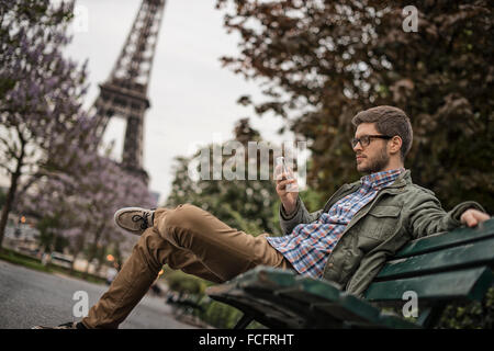 Ein Mann sitzt auf einer Parkbank in der Champs de Mars unter dem Eiffelturm. Stockfoto