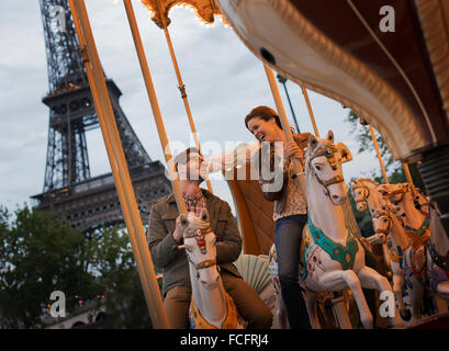 Ein paar, Mann und Frau auf traditionellen Gallopers auf einem Karussell fahren im Schatten des Eiffelturms in Paris. Stockfoto