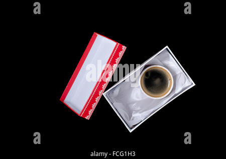 eine Tasse Kaffee in einer Geschenkbox auf schwarzem Hintergrund Stockfoto