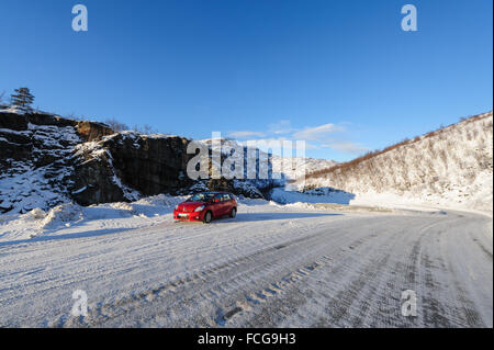 Ice auf einer Straße in Nord-Norwegen mit einem roten Auto am Straßenrand geparkt Stockfoto
