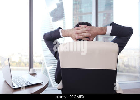 Geschäftsmann entspannt sitzen im Büro und im Fenster suchen Stockfoto