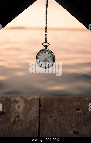 Taschenuhr und Kette auf Sonnenuntergang in der Nähe von Wasser. Stockfoto