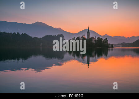 Kleine Insel mit ihn in Bled See, Slowenien bei Sonnenaufgang mit Schloss und die Berge im Hintergrund Stockfoto