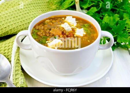 Linsensuppe mit Spinat, Tomaten und Feta-Käse in eine weiße Schale, Löffel auf ein Küchentuch, Petersilie auf dem Hintergrund-board Stockfoto