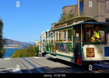 Cable Car an der Hyde Street an der Kreuzung mit der Lombard Street, mit Fernsicht auf der Insel Alcatraz, San Francisco, Kalifornien, USA Stockfoto