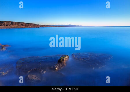 Untergetauchten Felsen in ein blaues Meer, unter freiem Himmel auf einem Bucht Strand am Sonnenuntergang. Pinienwald am Hintergrund Küste. Maremma, Toskana, Stockfoto