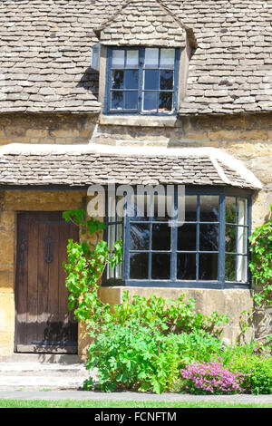 Alten englischen Cottage mit Braun aus Holz Haustüren, Fenster, umgeben von grünen Weinreben, Kräutern und rosa Blüten an heißen Sommertagen Stockfoto