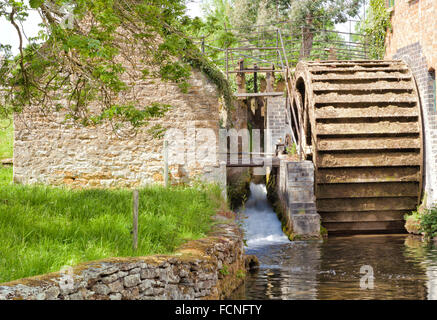 Alte steinerne Wassermühle mit hölzernen Wasserrad, kleiner Bach in ländlichen englischen Cotswolds Dorf Stockfoto