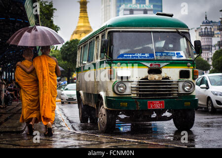 Alten Bus und zu Fuß unter dem Regen mit einem Regenschirm in Yangon, Mönche in der Nähe von Sule-Pagode. Myanmar Stockfoto