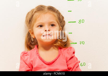 Kleines Mädchen, die Messung der Höhe gegen die Wand im Zimmer Stockfoto