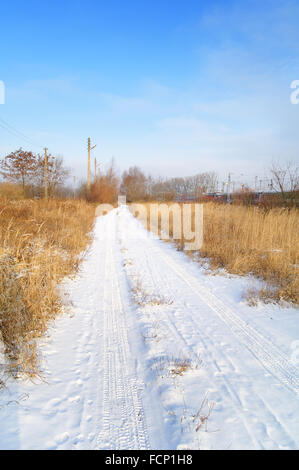 Schnee bedeckte Landstraße neben der Eisenbahn Stockfoto